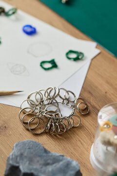 Vertical shot of metal key rings resting on worktable beside sketch paper and craft tools, supporting handmade product assembly. Useful for DIY branding, small business, retail supply
