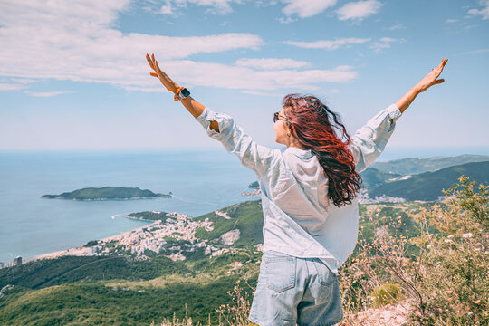 Joyful woman with arms outstretched, celebrating success and freedom with a scenic coastal town and blue sea in background