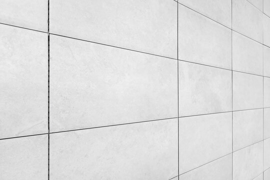 Minimalist white tile wall showing a linear grid of grout lines and subtle surface texture, photographed at an angle to create depth. Ideal as a modern architectural background or texture