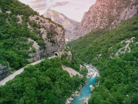 Winding road following Moraca river in a deep green valley with a tunnel cutting through the rugged mountain and rocky terrain in Montenegro