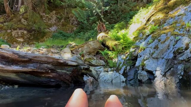 4K slow motion shot of a woman relaxing in the halfway hot springs beside a rushing mountain river, with crystal-clear water, dense conifer forest, and a peaceful wilderness setting.