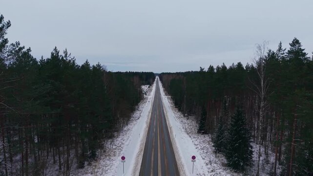 Drone ascends above the snowy P5 highway crossing Ogres Blue Hills, Latvia