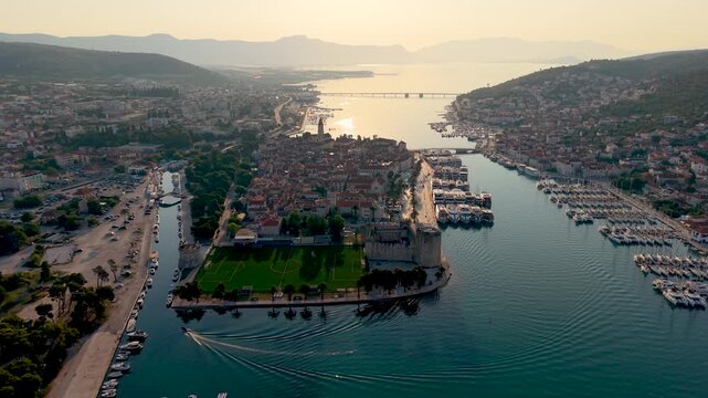 Croatia showcases the breathtaking charm of Trogir, where the sun sets over historical architecture and serene waters. Drone view of the old town with the football field