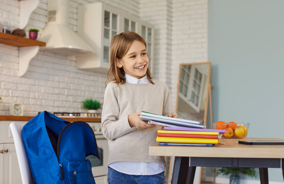 Portrait of little schoolboy preparing his schoolbag for school lessons putting textbooks. Smiling child boy packing backpack at home. Back to school, knowledge and education concept.
