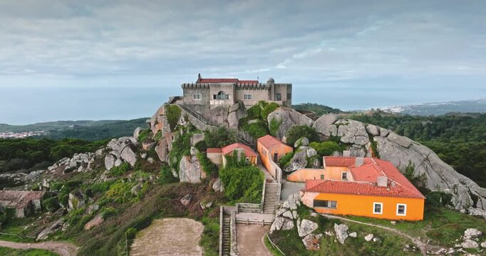 Aerial panorama of historic Sanctuary of Peninha complex on rocky peak overlooking the Atlantic Ocean, featuring ancient buildings nestled among rugged landscapes and lush greenery of Sintra, Portugal