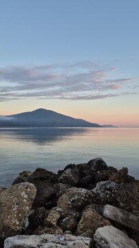 Albania welcomes you to Orikum, where tranquil waters meet stunning mountain views. Witness a picturesque sunset from the coastline, with boats gently swaying in the harbor.