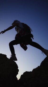 Silhouette of woman jumping across rocky gap at sunset. Courage, resilience, overcoming challenges, personal growth, achievement and success concept.