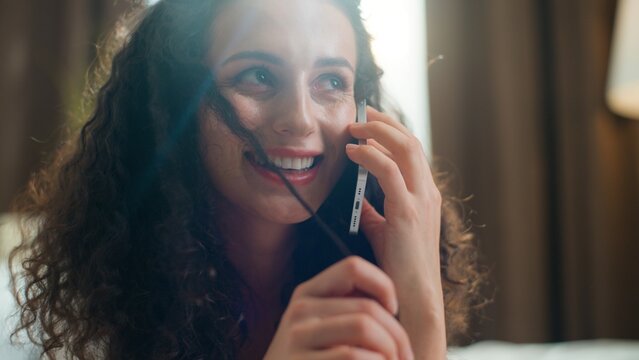 Happy Caucasian woman talking call with mobile phone with friend smile at cozy bed at home morning optimistic female girl talk smartphone chatting conversation laughing smiling at comfortable bedroom