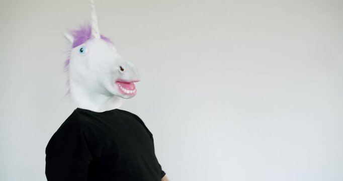 A man wearing a unicorn mask dances in a studio with a plain white background. He is having fun and not taking himself too seriously, enjoying the absurdity of the situation.