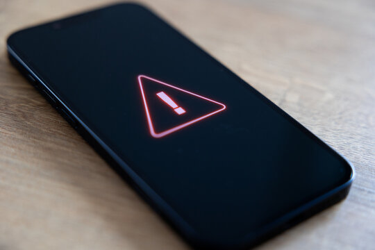 Smart phone screen shows system warning sign, computer crime, system hacked. Network security, firewall, samrtphone virus, data, privacy, safety, danger, data breach, computer problems.