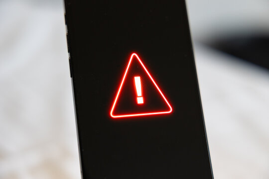 Smart phone screen shows system warning sign, computer crime, system hacked. Network security, firewall, samrtphone virus, data, privacy, safety, danger, data breach, computer problems.