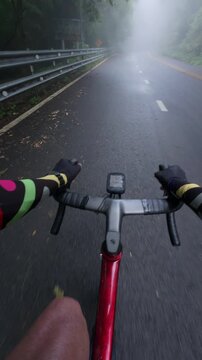 First-person point of view of a road cyclist riding into dense fog along a wet mountain road surrounded by tropical forest. The immersive footage captures low-visibility riding, misty weather, rain-so