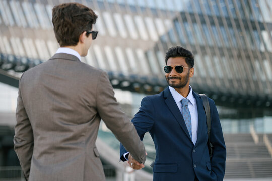 Indian businessman shaking hands with colleague outside office building, signaling partnership and corporate success. Ideal for business networking, recruitment, leadership campaigns