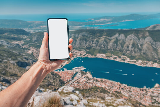 Hand holding modern smartphone with blank screen for travel app integration, viewing the scenic Bay of Kotor, Montenegro