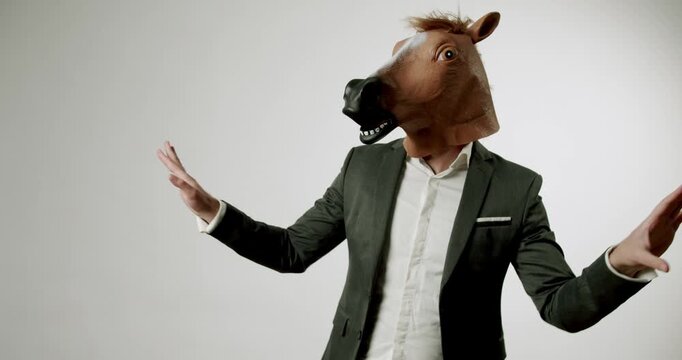A man in a suit wearing a horse head mask is dancing against a white background. He looks funny, weird, and strange. This video is perfect for any project that needs a touch of the absurd.