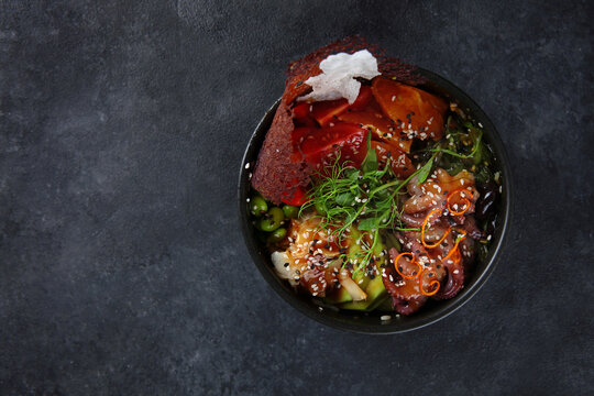 Poke with octopus, avocado, and tomatoes. A traditional Hawaiian dish. Dark background. Top view. Copy space