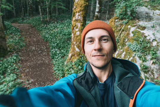 Young man smiling during a selfie, experiencing nature while hiking a vibrant green trail through a broadleaf forest