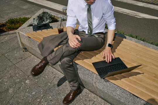 High angle view of young adult businessman working on laptop while sitting outdoors, using flexible workspace for mobile productivity. Ideal for remote work, business mobility marketing