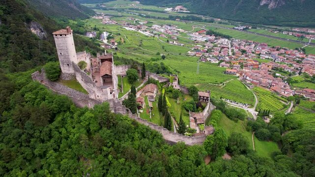 Castello di Avio medieval castle drone view Trentino Italy. Aerial panoramic flight over ancient ruined fortress on hill top among dense green forest high above valley town landscape. 4K