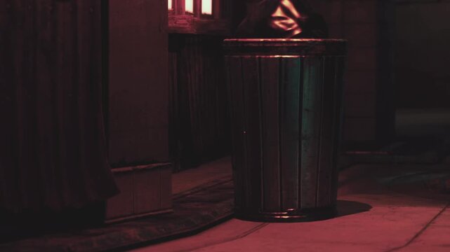 A trash can stands in an alleyway. Colorful lights reflect off its surface. The scene takes place at night with shadows around. This area shows urban life and discarded items.