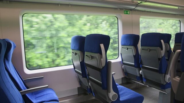 Blue seats inside modern moving train carriage with large windows showing blurred green landscape