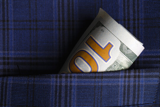 Close-up of a rolled U.S. dollar bill tucked into a blue plaid fabric pocket, highlighting concepts of savings, finance, and security.