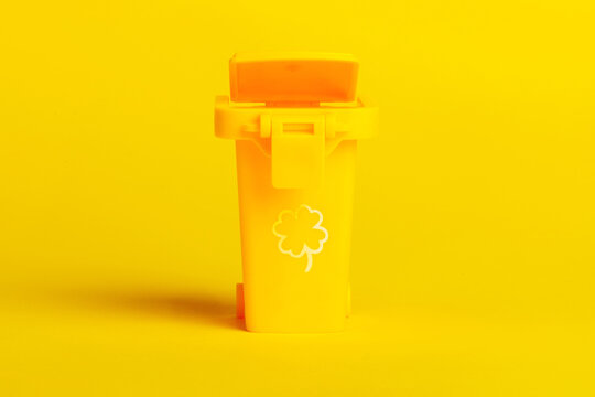 Minimalist yellow trash bin with clover icon, isolated on vibrant yellow background. Modern waste management and eco-friendly concept.
