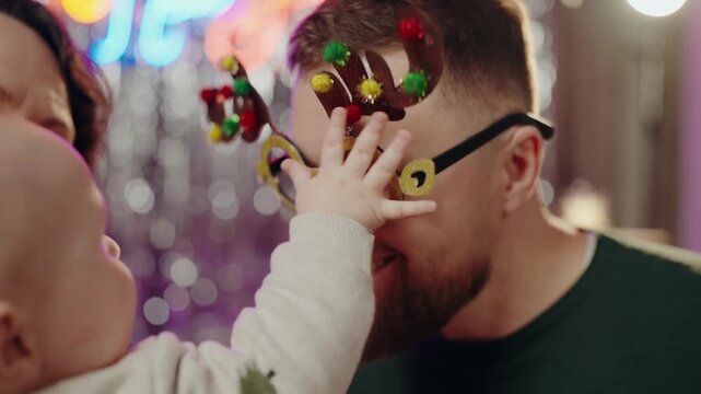 A joyful father and his baby celebrating Christmas together. The father is wearing festive reindeer antler glasses, creating a fun and memorable holiday moment. Father and Baby Celebrating Christmas