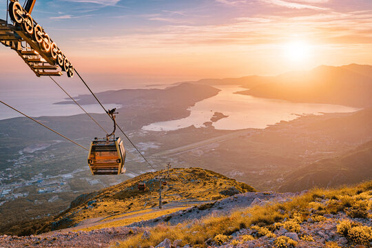 Cable car ascending rugged mountain slope with a dramatic sunset illuminating the Bay of Kotor and the Adriatic Sea below