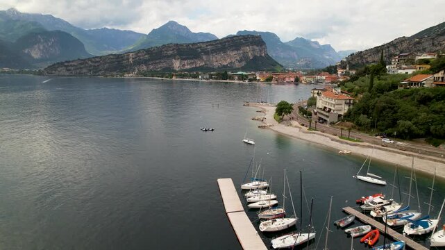 Torbole Lake Garda Italy 4K Drone. Aerial flight over sailboat marina to village. Colorful houses waterfront with alpine mountains background scenic Trentino travel b roll cinematic video asset