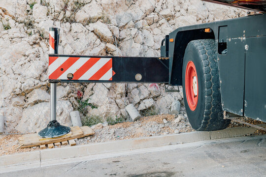 Industrial equipment with red and white safety stripes deployed, providing stability for a construction crane near a rocky area