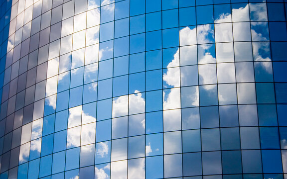 Clouds reflected in modern glass skyscraper windows. Vibrant blue sky reflection on curved corporate office building facade.