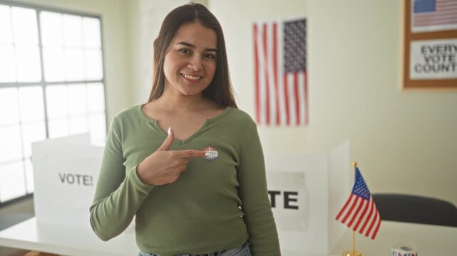 Woman pointing finger to 'i voted' sticker on chest inside a polling station building with voting booth and american flag visible; pride civic duty.