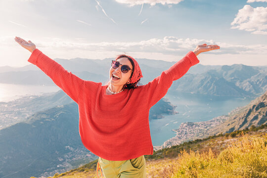 Smiling woman with arms outstretched celebrating happiness and well being during travel in the mountains of Montenegro