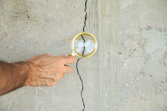 Male hand with a magnifying glass checking a cracked wall after earthquake.