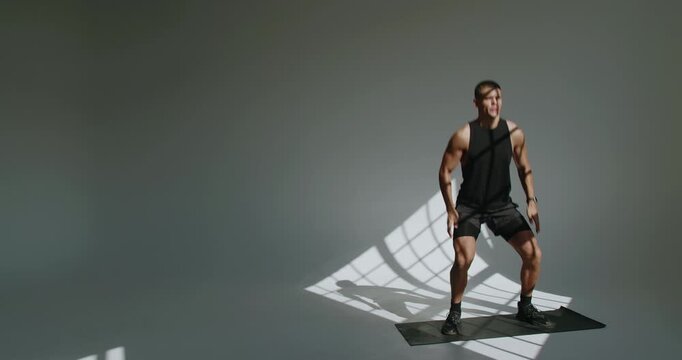 Athletic man engages in fitness exercises in a studio with striking shadow patterns on the wall. Young Athletic Man Training in a Studio, Shadow Patterns on Wall