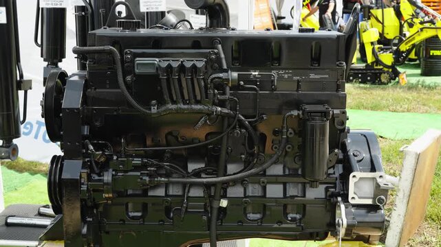 A brand new black diesel engine with an attached clutch assembly stands on a wooden frame at an outdoor exhibition.