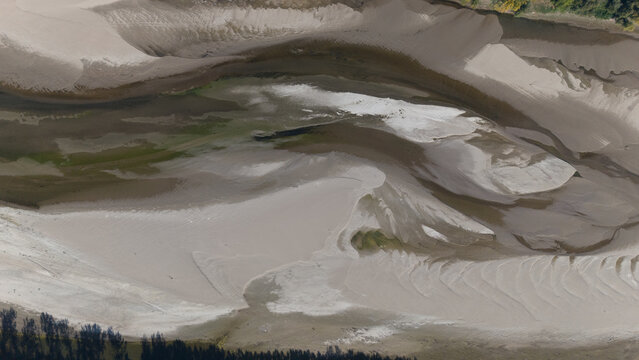 An abstract aerial perspective reveals the intricate patterns of a parched riverbed, showcasing sandbars and patches of green growth