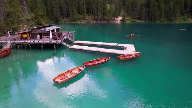 Lago di Braies Italy 4k drone tracking view of wooden boats on turquoise lake. Aerial reveal of Pragser Wildsee in Dolomites mountains South Tyrol alpine background b-roll establishing stock video