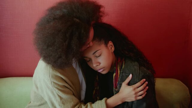 A woman with curly hair holds a child on her lap who is asleep or resting. The adult seems to be providing emotional support.