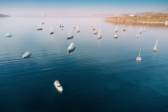 Aerial view of luxury yachts, sail boats, and catamarans on calm turquoise sea in Bodrum, Turkey, with coastline in background