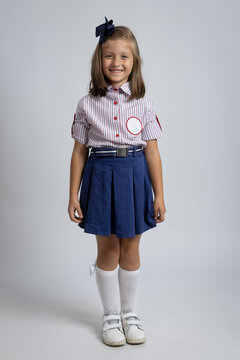 Smiling little schoolgirl in school uniform standing in studio, happy child portrait. Education and childhood concepts. Back to School