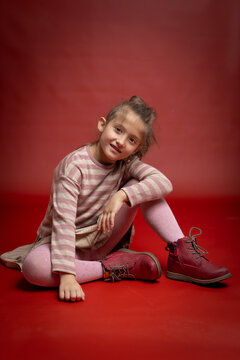 Cute Smiling Little Girl Sitting on Red Background. Playful Child Fashion Portrait