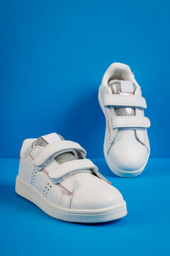 Stylish white kids' sneakers with velcro straps on blue background. Children's fashion footwear for active play and back to school concept.