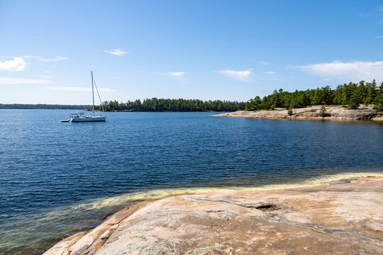 A serene view of a sailboat on the blue waters of Killbear Provincial Park, Ontario, with rocky shores and dense forest in the backdrop.