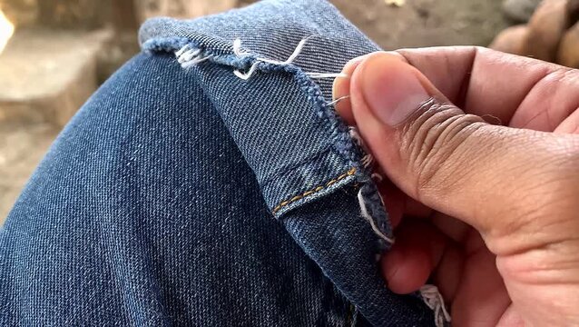 Close up of a hand holding frayed blue denim jeans with loose white threads. Classic style and ruggedness.