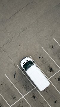 Minimal aerial abstraction of a single white car parked in an empty marked lot