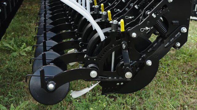 A close-up shot focuses on the intricate row units and disc openers of a modern black agricultural seed drill.