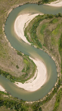 Aerial abstraction of a meandering river carving an S curve through green banks