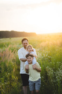 Happy father spending quality time with his two children in a blooming summer meadow during golden hour. Authentic family lifestyle, fatherhood, Father's Day celebration, childhood, bonding.
